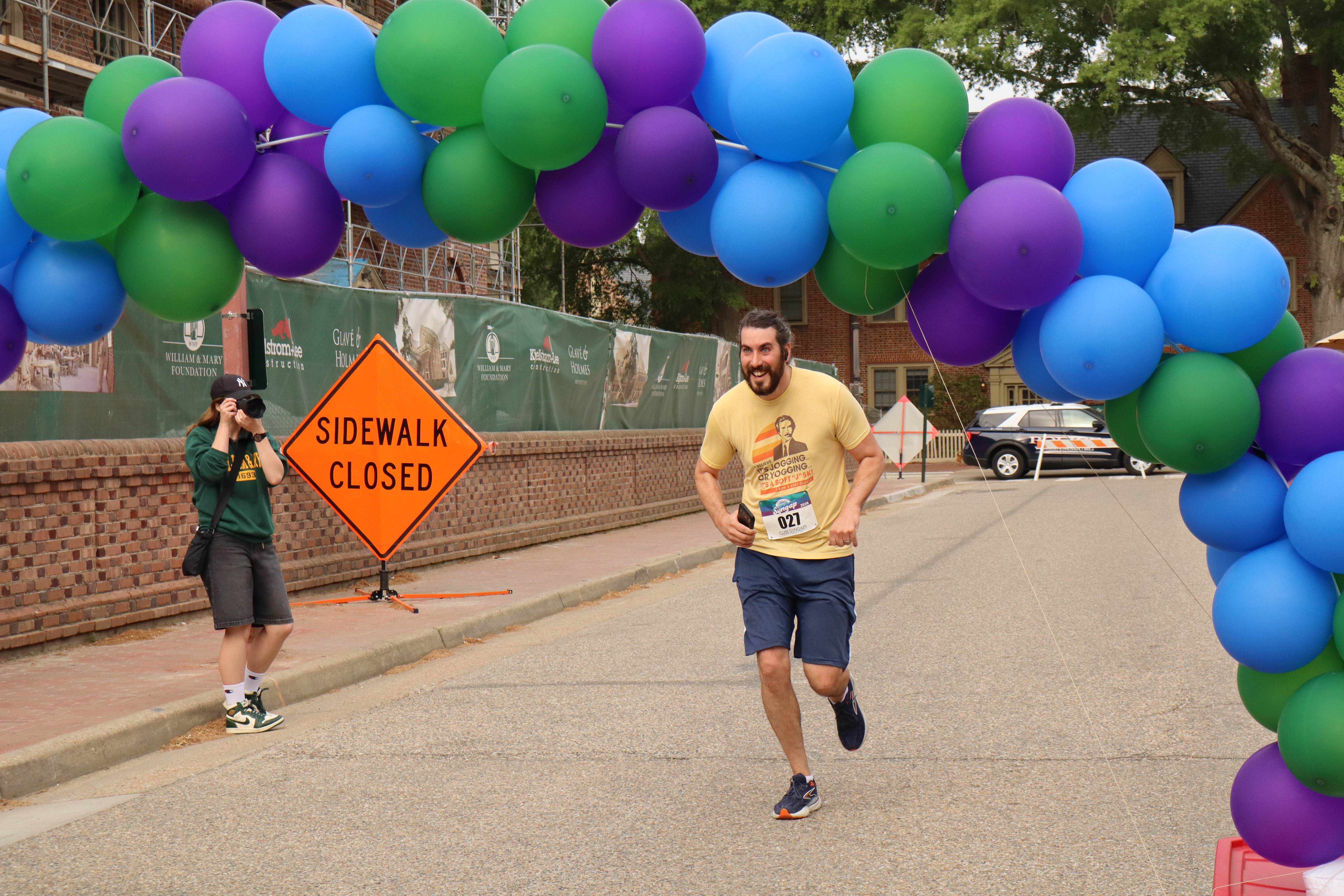 Runner crossing beneath the colorful balloon arch at the 2026 Mora and Qusay 5K
